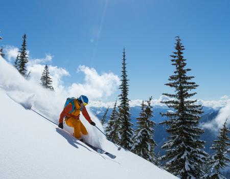 man skiing down mountain with fresh snow flying by him