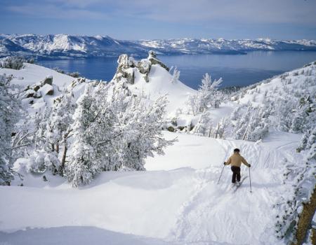 A person skis down a snowy mountain's groomed slope overlooking Lake Tahoe